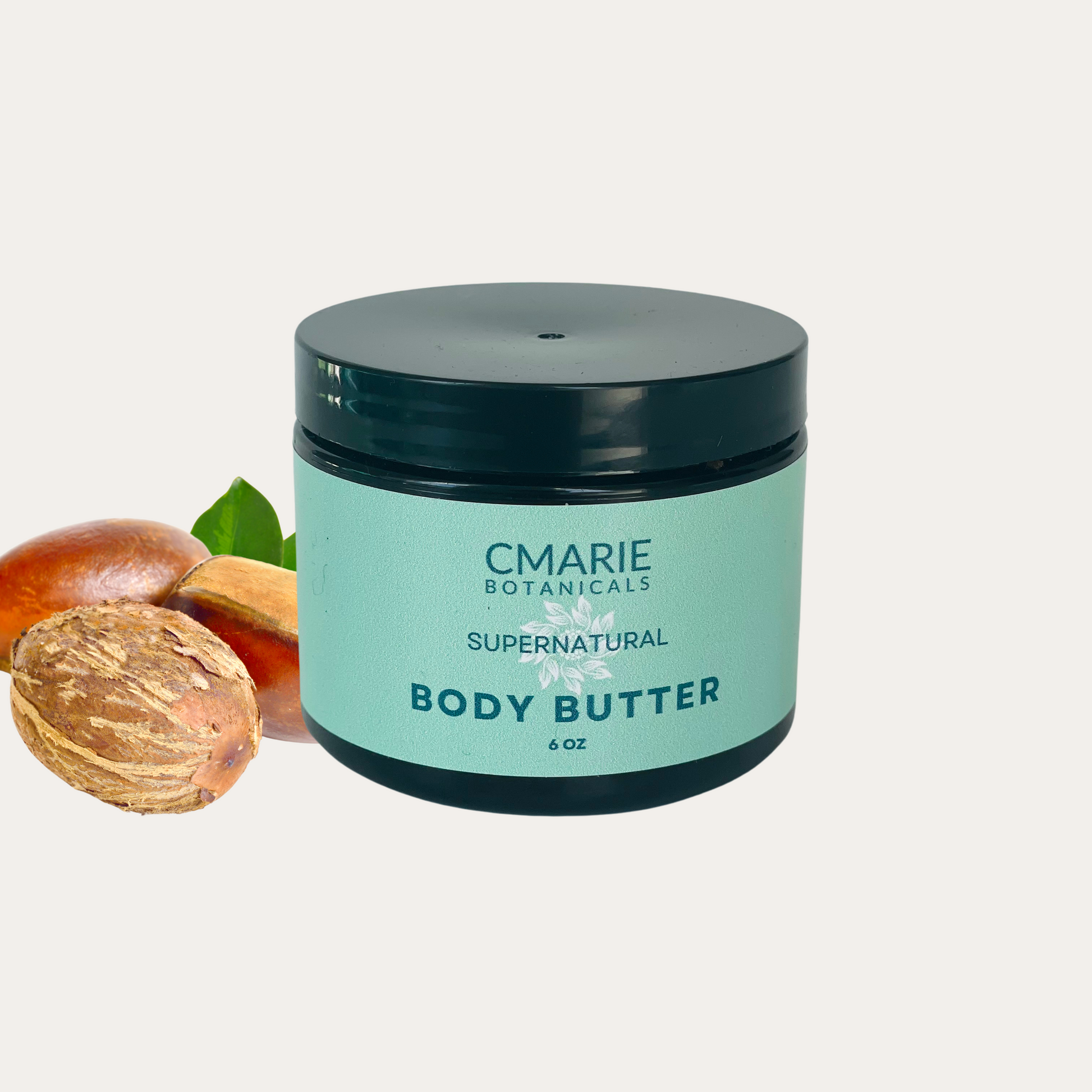 C Marie Botanicals Supernatural Body Butter in an amber 6.0 oz container with mint green label. The product is accompanied by fresh, shea nuts, emphasizing its natural and organic ingredients.