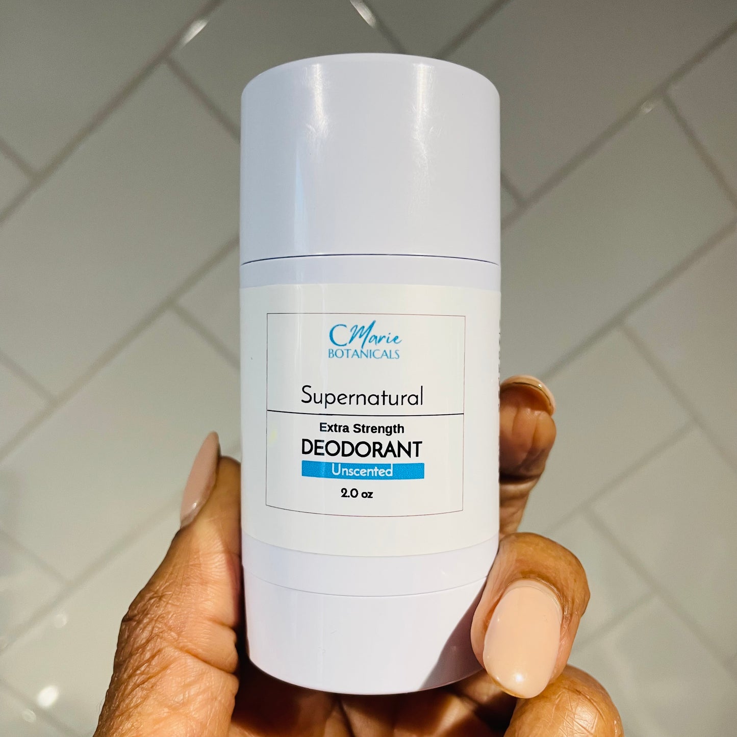 Image of C Marie Botanicals Supernatural Deodorant, a natural deodorant Unscented in a sleek white 2.0 oz container. The product is being held by hand.